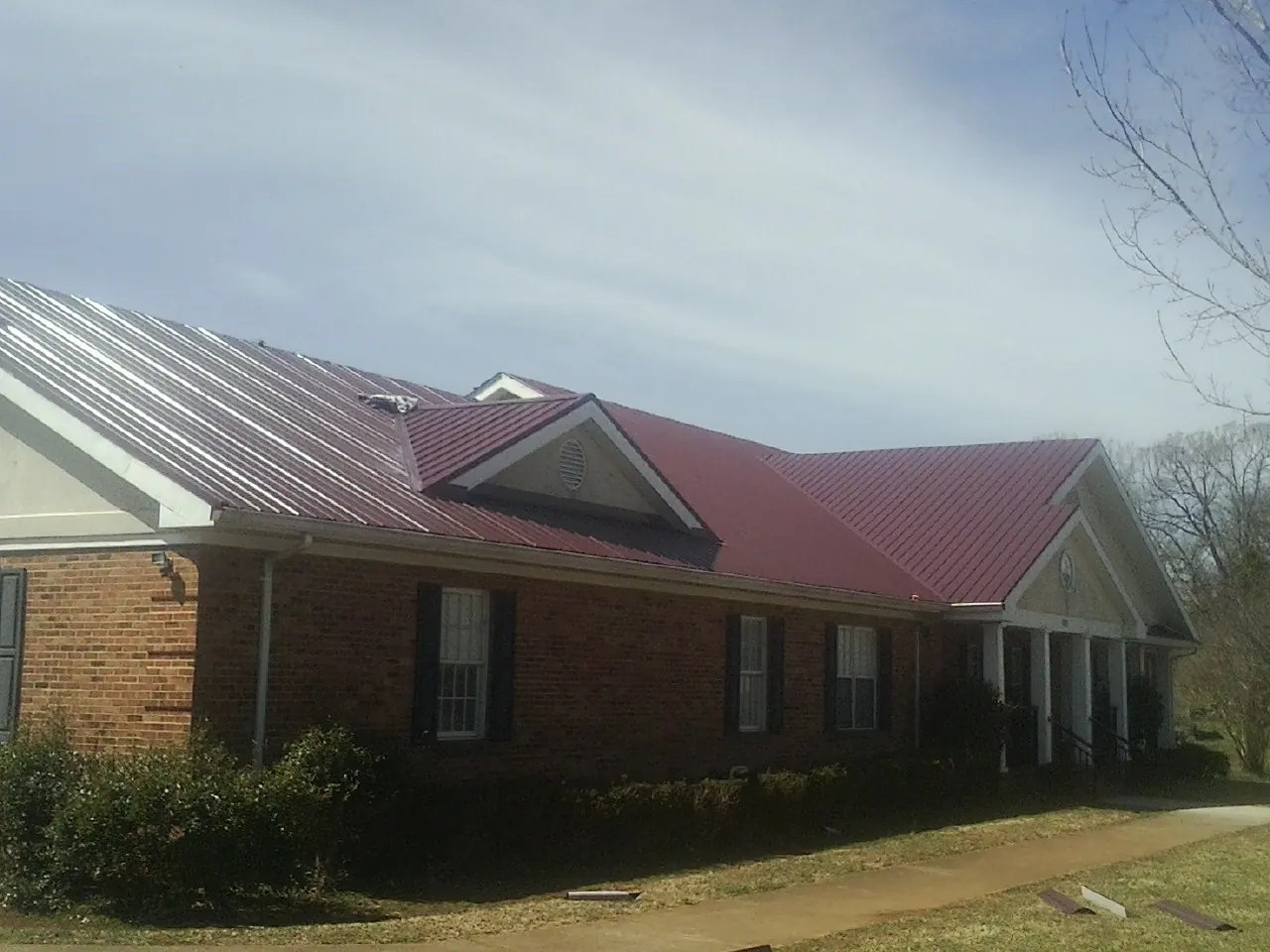Red metal roof with gabled entries on a long brick building, from a Hail Damage Roof Repair job in Vona
