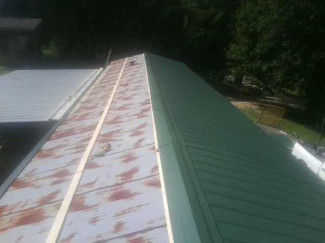 Old rusted panels beside newly installed green metal roofing — Wind Damage Roof Repair by Roofing Brothers in Vona