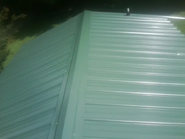 New green metal panels meeting at the ridge of a roof — Flat Roof Repair work by our crew in Vona