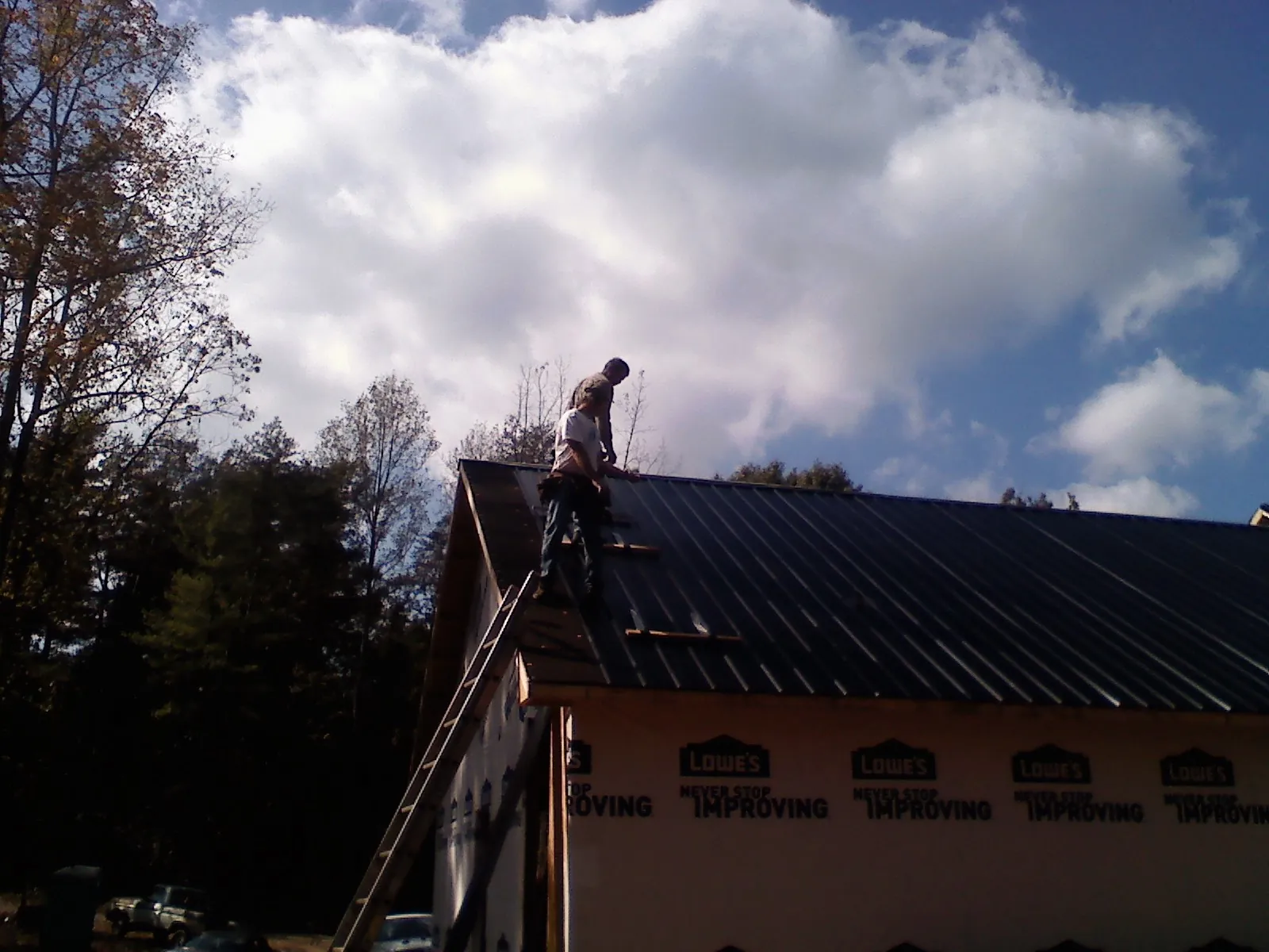 Roofer fastening dark metal panels high against a cloudy sky, from a Roof Inspection job in Vona