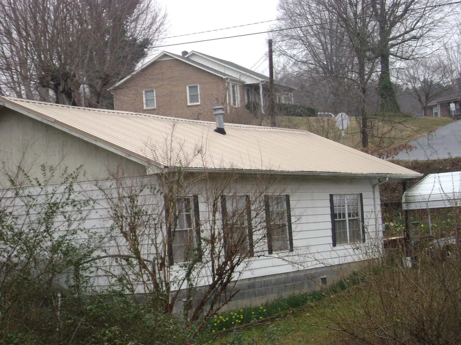 Tan metal roof on a white sided house set into a hillside — Commercial Roofing by Roofing Brothers in Vona
