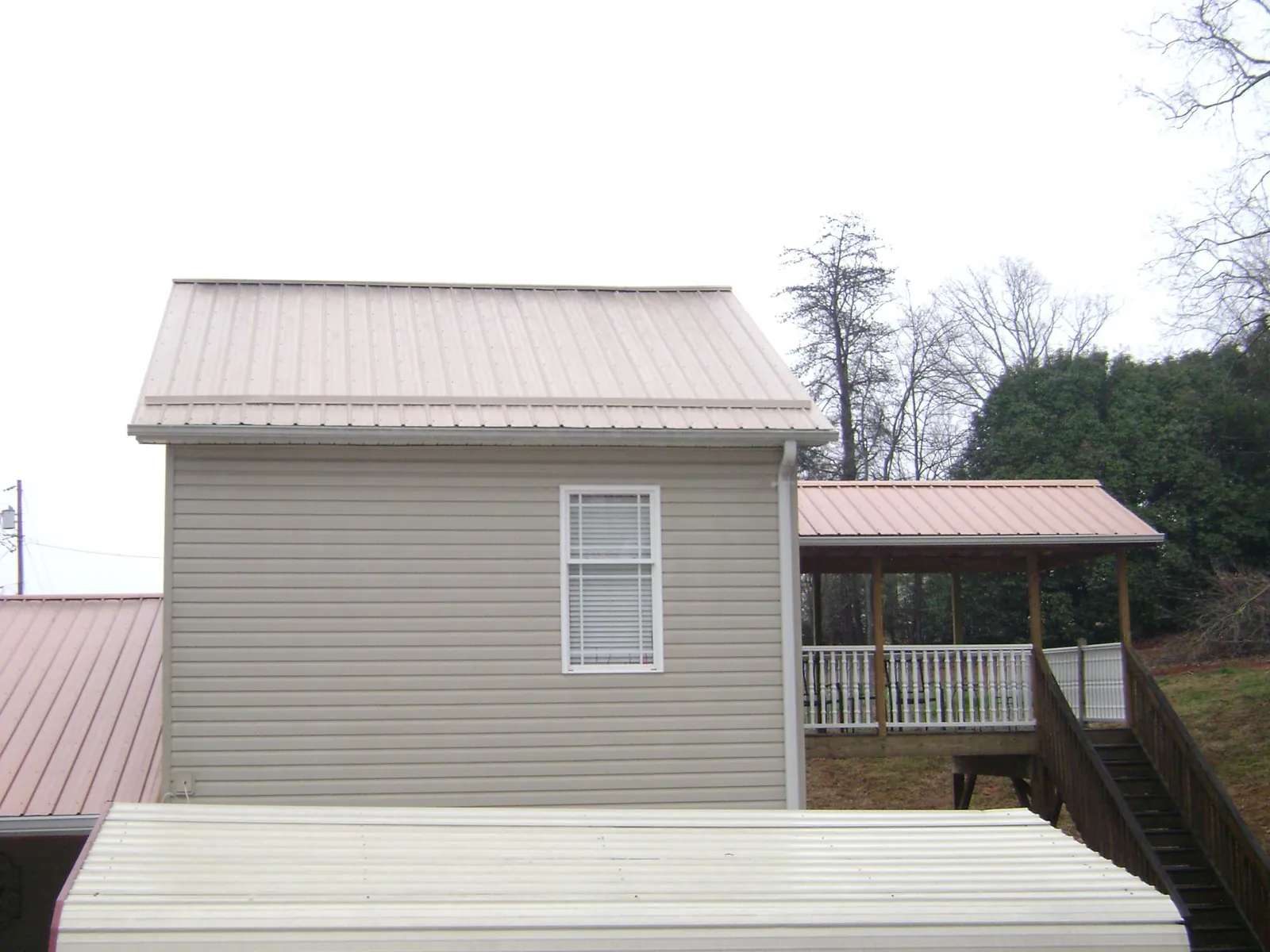 Tan metal roofs on a two story addition and attached porch, from a Roof Replacement job in Vona